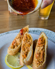 Spring rolls stuffed with marlin, on a white plate with macha salsa macha on top.