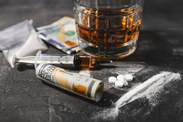 White narcotic pills, an alcoholic drink in a glass, a syringe with a dose of heroin, a line of...