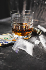 White narcotic pills, an alcoholic drink in a glass, a syringe with a dose of heroin, a line of cocaine powder and US dollar bills on a dark background. Concept of addiction and bad habits