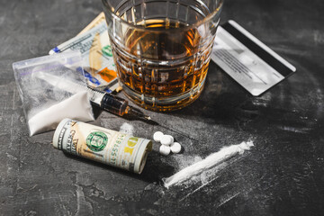 White drugs, narcotic pills, an alcoholic drink in a glass, a syringe with a dose of heroin, a line of cocaine powder and US dollar bills on a dark background. Concept of addiction and bad habits