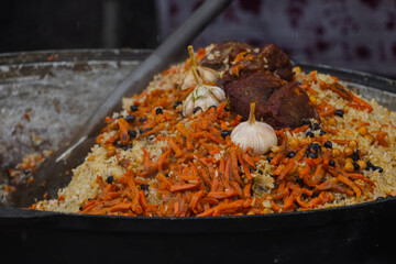 pilaf in an iron cauldron with onions, garlic, carrots, meat and vegetables, street food