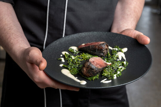 the chef is holding a plate of deer steak, with spinach. Michelin chef, luxury dishes.