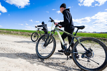 Naklejka premium A picturesque scene of two young cyclists on mountain bikes, enjoying a leisurely ride along a country road under a bright blue sky. The setting suggests a rural area.