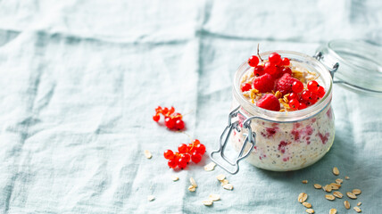 Overnight oats with fresh raspberries and red currants in glass jars. Blue textile background. Copy space.