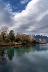 Fototapeta premium landscape on a lake with trees against clouds in alpine foehn light in autumn / fall or winter with high mountains in background