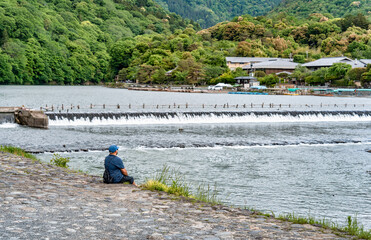 Obraz premium Single unidentifiable man sitting on the bank of Katsura river in Arashiyama district, Kyoto.