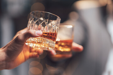 Whiskey Toast: Two hands clinking glasses of amber whiskey, a warm, intimate moment captured in soft focus.  A toast to friendship, celebration, or a successful deal.
