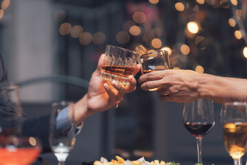 Toasting Success: Close-up shot of two hands clinking glasses of amber liquid, celebrating a successful business deal or a special occasion in an elegant setting.  