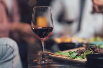 A Toast to Good Times: A close-up of a single glass of red wine, a symbol of celebration and relaxation, sits in the foreground, with friends enjoying a meal and conversation in the background.  