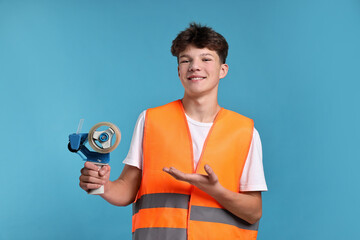 Teenage boy with tape gun dispenser in safety vest working as warehouse packer on blue background