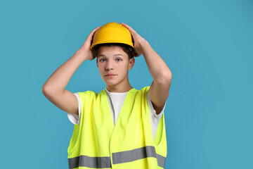 Teenage boy in hardhat and safety vest working as builder on blue background