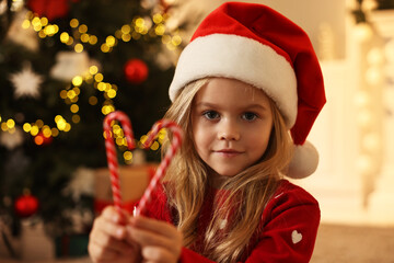 Little girl in Santa hat with candy canes at home. Christmas celebration