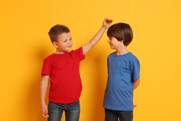 Cute brothers comparing their height on orange background