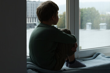 Autism concept. Lonely little boy near window at home