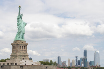 The Statue of Liberty on the Liberty Island with the Jersey City skyline in the background.