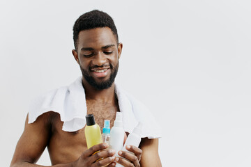Shirtless man holding lotion and conditioner bottles, implying skincare and haircare routine in a...