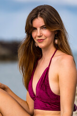 Redhead Bikini Model Basks in Spring Sun by Majestic Rocks and Shimmering Marina, with Endless Blue Sea Beyond