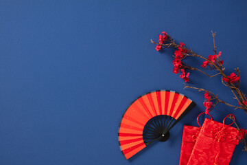 Chinese New Year 2025 flat lay with red packets, paper fan, sakura branch on blue background