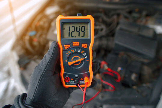 Man using multimeter to measure car battery voltage level during winter maintenance, alternator producing 12.49 volts with engine idling, bad alternator. Alternator malfunction
