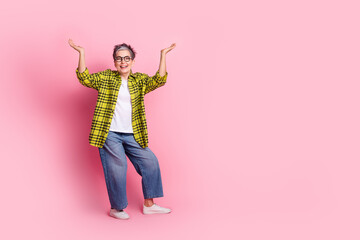 Full body portrait of pretty aged lady arms hold empty space isolated on pink color background