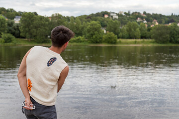 Junger Mann aus Indien steht am Fluss und wirft Steine ins Wasser