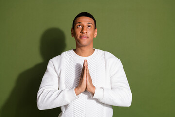 Young man in a white sweater with a charming look holding hands in a contemplative prayer pose against a khaki background