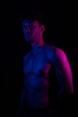 Naklejka premium Junger Mann aus Indien steht mit freiem Oberkörper in buntem Licht und posiert