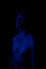 Junger Mann aus Indien steht mit freiem Oberk&ouml;rper in buntem Licht und posiert