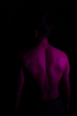 Junger Mann aus Indien steht mit freiem Oberk&ouml;rper in buntem Licht und posiert