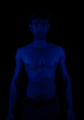 Naklejka premium Junger Mann aus Indien steht mit freiem Oberkörper in buntem Licht und posiert