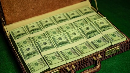 Brown briefcase full of one hundred dollar bills on green background