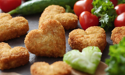 Heart-shaped nuggets snacks arranged with fresh vegetables and cherry tomatoes on a dark stone surface. Valentine&rsquo;s Day idea, date, engagement party, love party, eat, food