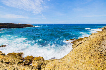 Rocky coastline of Arikok National Park in Aruba with turquoise Caribbean Sea waves crashing against rugged cliffs.