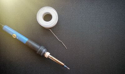 An electric soldering iron with a metal tip and a coil of wire on a dark background. Soldering of...