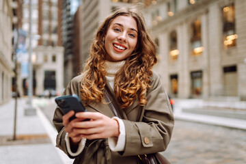 Obraz premium Portrait of happy woman with smartphone in the street city. Concept of vacation, blogging, technology, weekend.