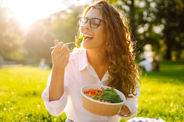Young woman enjoying a healthy meal. Beautiful woman eating fresh vegetable salad outdoor. Vegetarian.