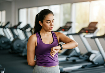 Young woman checking smartwatch during fitness training in modern gym