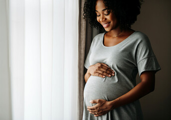Happy pregnant woman holding her belly near the window, enjoying pregnancy time at home