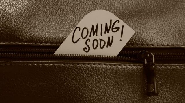 Text Coming Soon on paper. Close up of zip on dark textured leather. Grunge style	