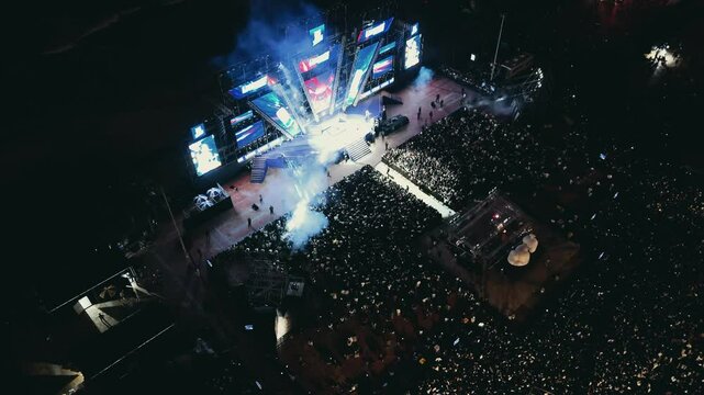 Open air music concert festival. Massive crowd gathering for night event near coastline. Colorful stage lighting illuminating energetic music performance with dynamic visual effects