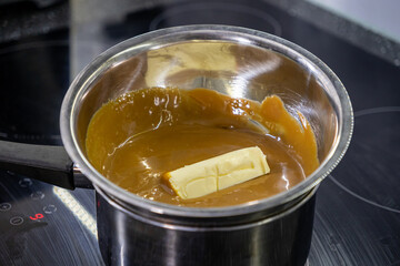 Melting butter in a pot of caramel sauce on a stovetop, dessert preparation process in close-up view