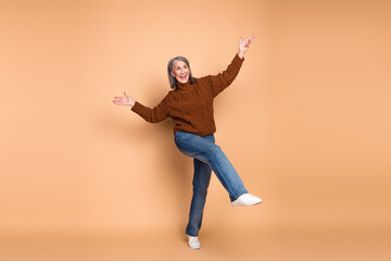 Happy elderly woman in brown sweater striking playful pose against beige background