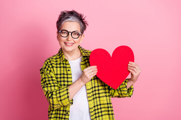 Portrait of pretty aged lady hold red paper heart plaid shirt isolated on pink color background