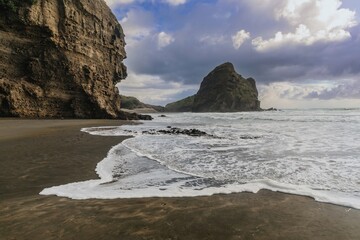 Powerful waves crash on a dark sand beach, dramatic cliffs loom in the background. Nature's raw...