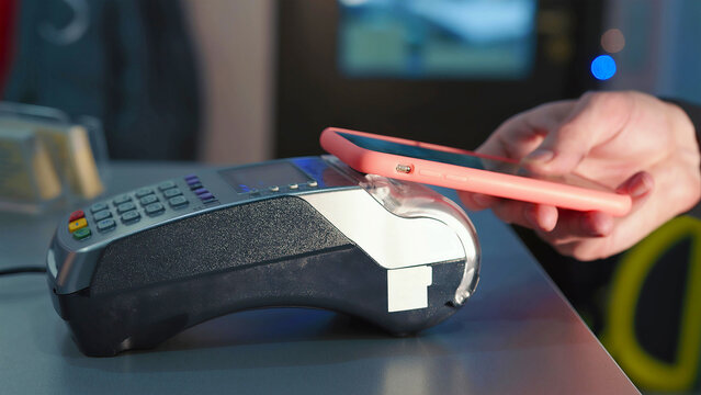 Contactless Payment with Smartphone at Terminal. Close-up of a hand holding a smartphone making a contactless payment on a card reader, illustrating modern digital transactions.
