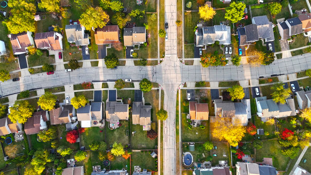 Aerial View of Suburban Neighborhood in Autumn. Top-down aerial shot of a suburban neighborhood with neatly arranged houses, driveways, and colorful autumn trees lining the streets.