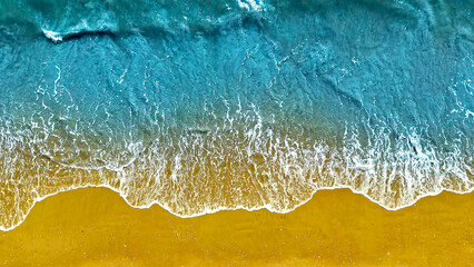 Aerial View of Ocean Waves on Sandy Beach. Top-down view of turquoise ocean waves gently crashing onto a golden sandy beach, creating a vibrant and serene coastline.