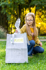 Little girl picking up trash outdoors sorting plastic waste into recycle bags