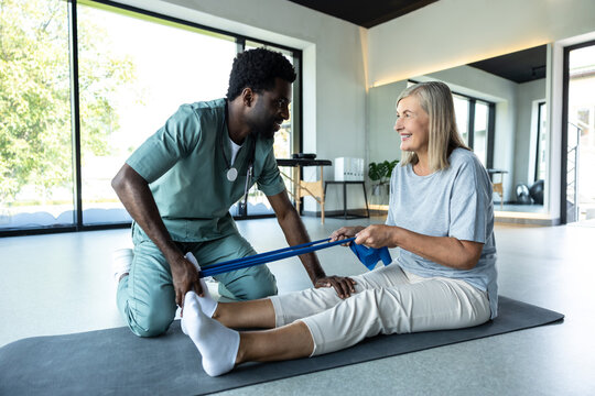 Man physiotherapist guiding woman through leg exercise with resistance band for muscle recovery