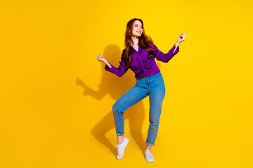 Fototapeta premium Photo portrait of beautiful young red hair curls lady in violet shirt and jeans dancing model isolated on yellow color background